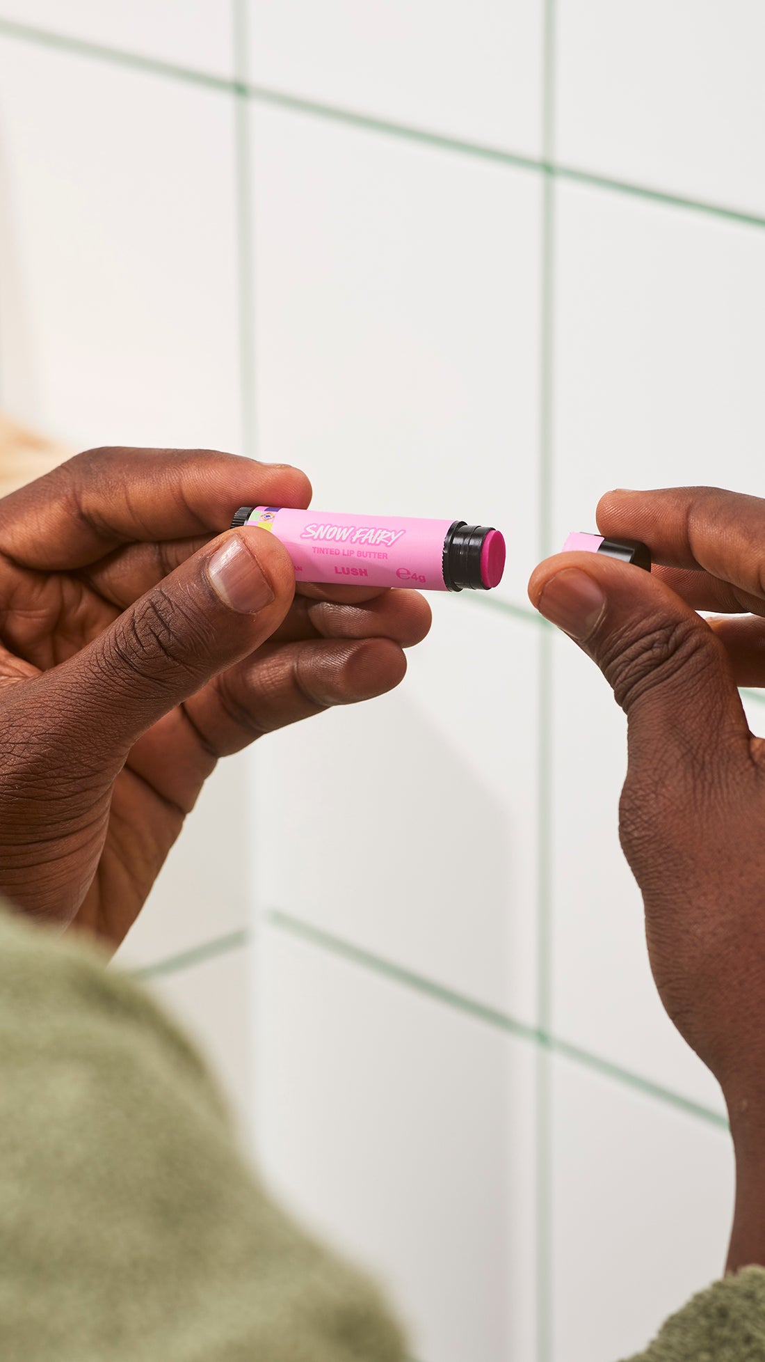 Hands remove the black cap from a pink Snow Fairy lip balm tube.