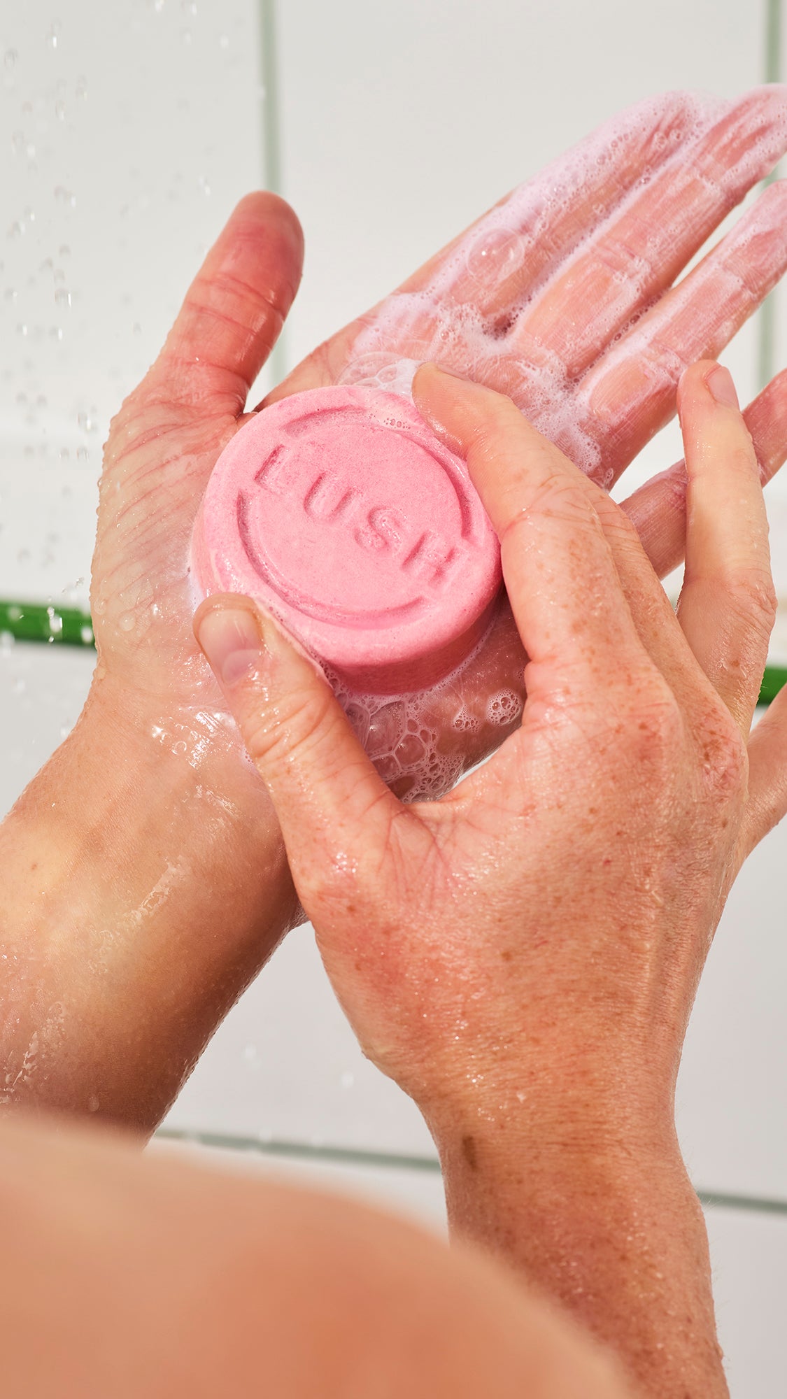 Lathered hands hold a round pink Snow Fairy shampoo bar stamped with Lush lettering.