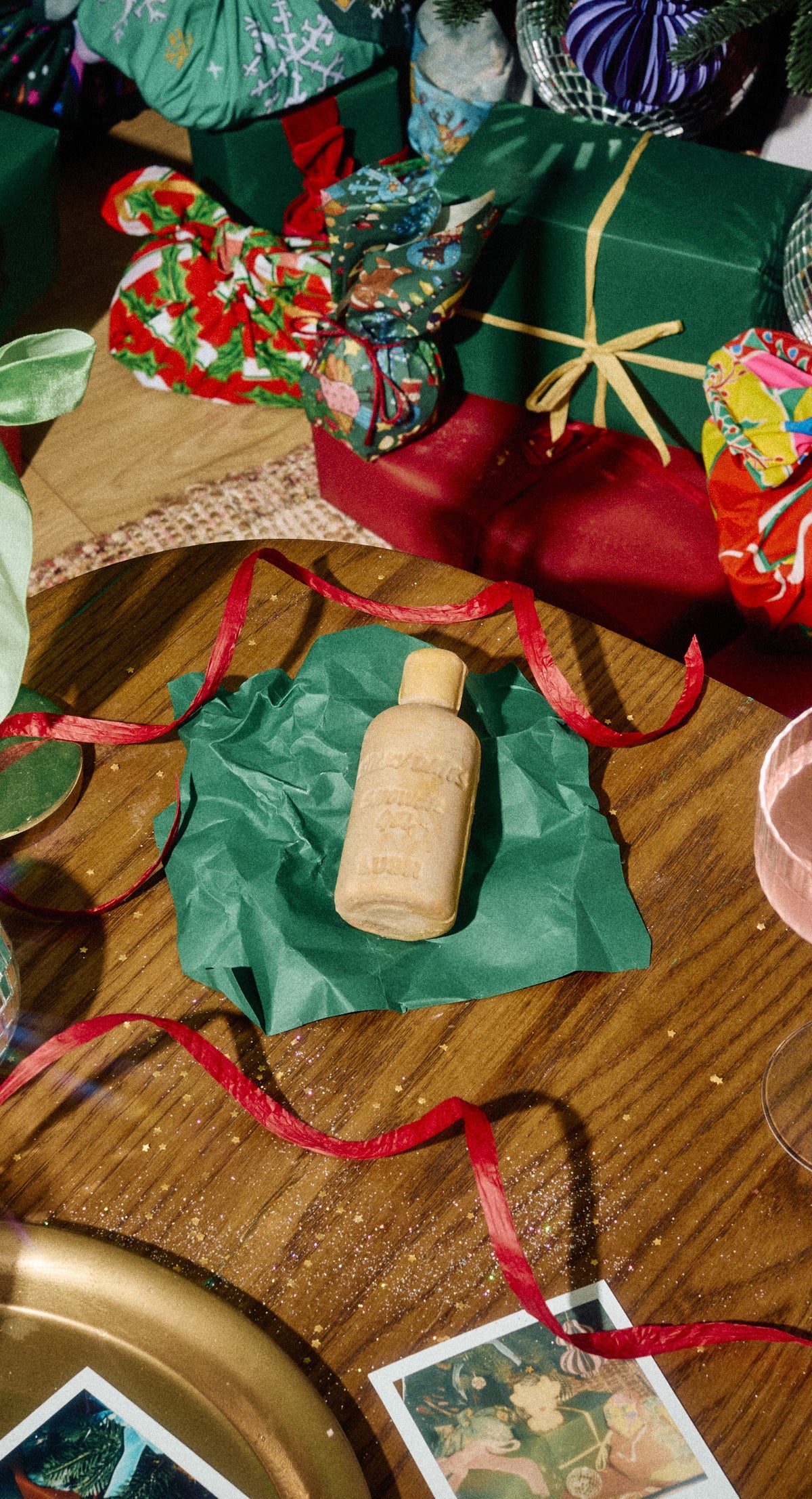 Bottle-shaped tan Sticky Dates naked shower gel rests on green wrapping paper beside Christmas gifts.