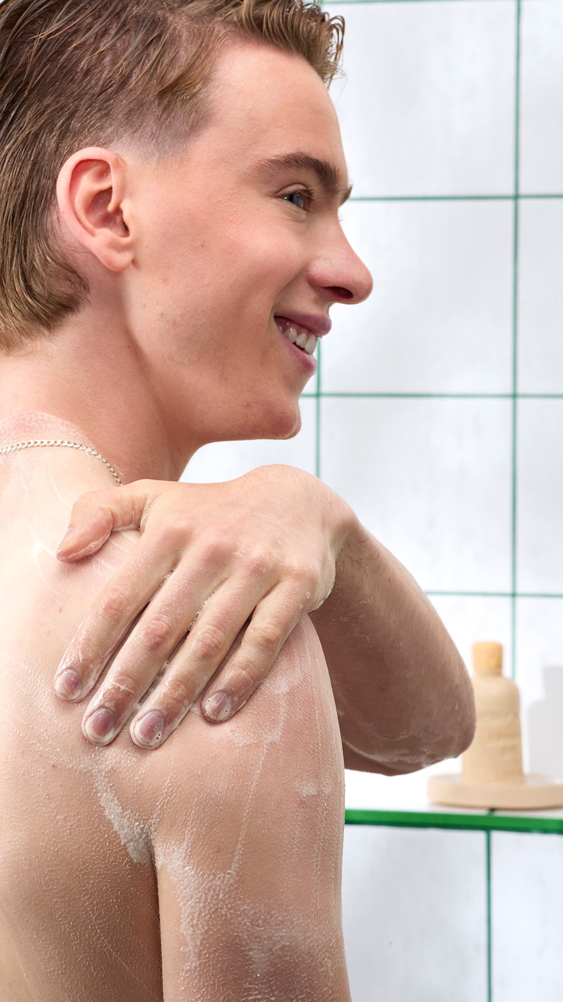 A smiling person rubs Sticky Dates shower-gel lather over their shoulder.