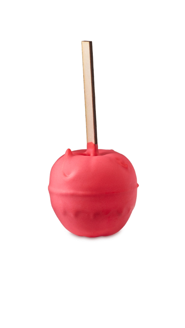 A red apple-shaped bath bomb with a long wooden stick inserted on the top. 