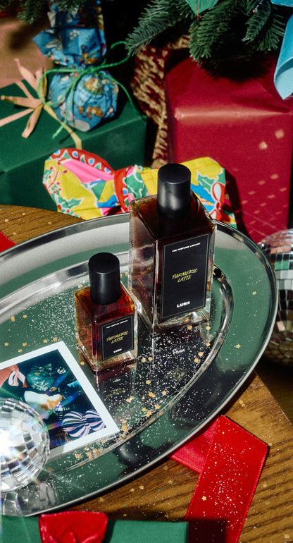 Two sizes of Turmeric Latte perfume in rectangular glass bottles displayed on a silver festive tray.