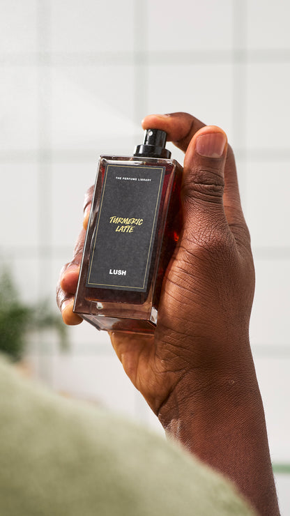 Close-up of a hand holding a rectangular Turmeric Latte perfume bottle with its spray exposed.