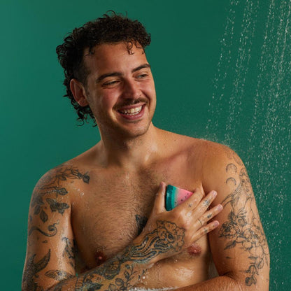 A super-close-up image of the model on a bright yellow background as they smooth the Watermelon Slice soap over their chest, creating a rich, soapy lather.