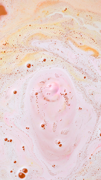 Pale pink, orange and white Yog Nog bath-bomb foam swirls across the water.