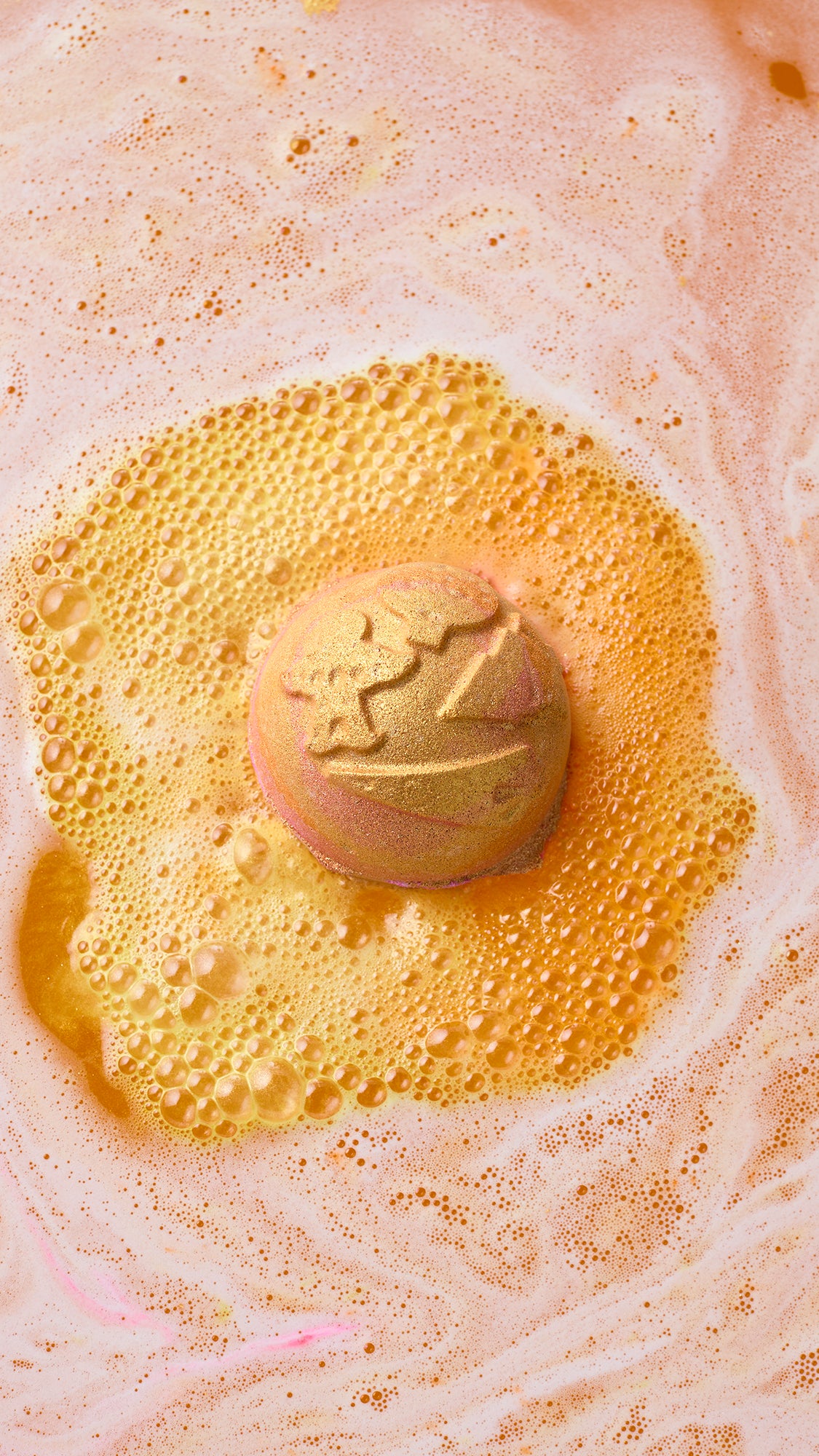 A round Yog Nog bath bomb with an embossed design surrounded by golden-orange foam.